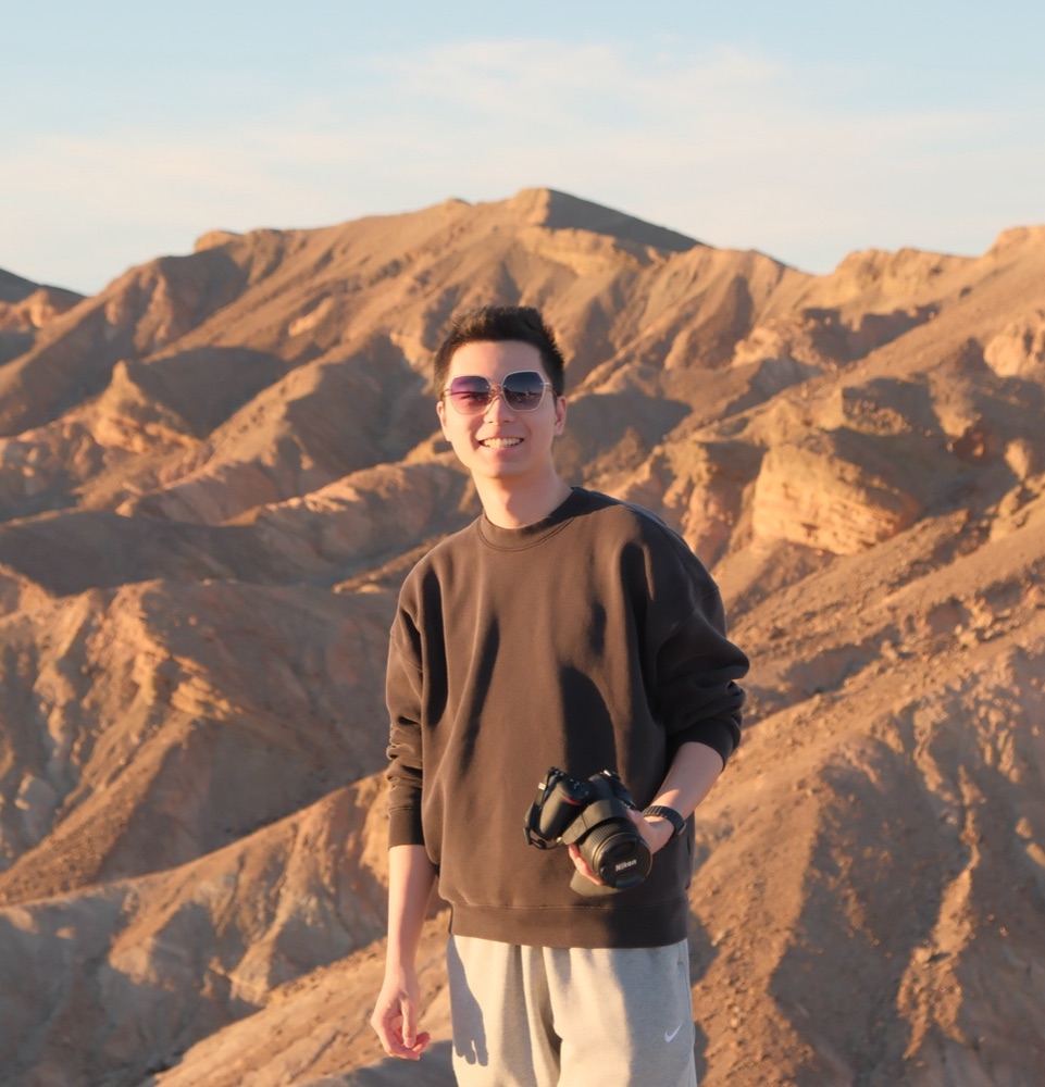 Yixuan Yang standing on a ridge in Death Valley, holding a camera